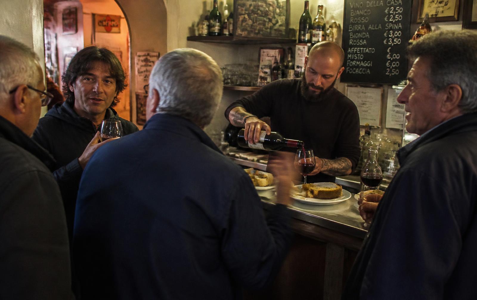Gäster vid en liten italiensk bardisk på kvällen, bartendern häller upp, focaccia på tallrikar